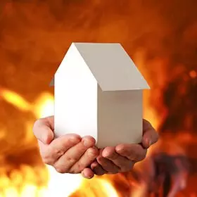 Hände halten ein Modellhaus, brenndener Hintergrund